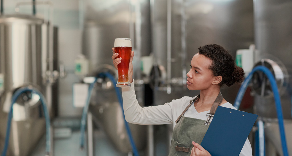 Maestra cervecera mirando un vaso de pinta en una fábrica de cerveza